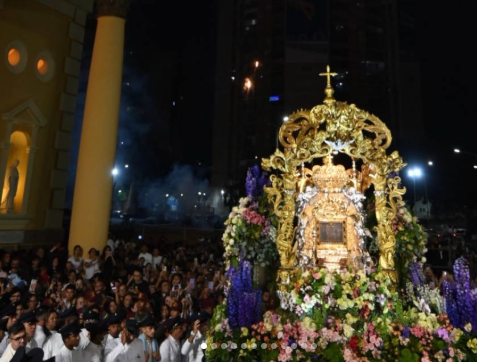 Imagen nocturna de la Virgen de Chiquinquirá (La Chinita) en su procesión. La imagen está sobre un trono dorado barroco y rodeada de una profusa decoración floral. Una multitud de devotos asiste al evento